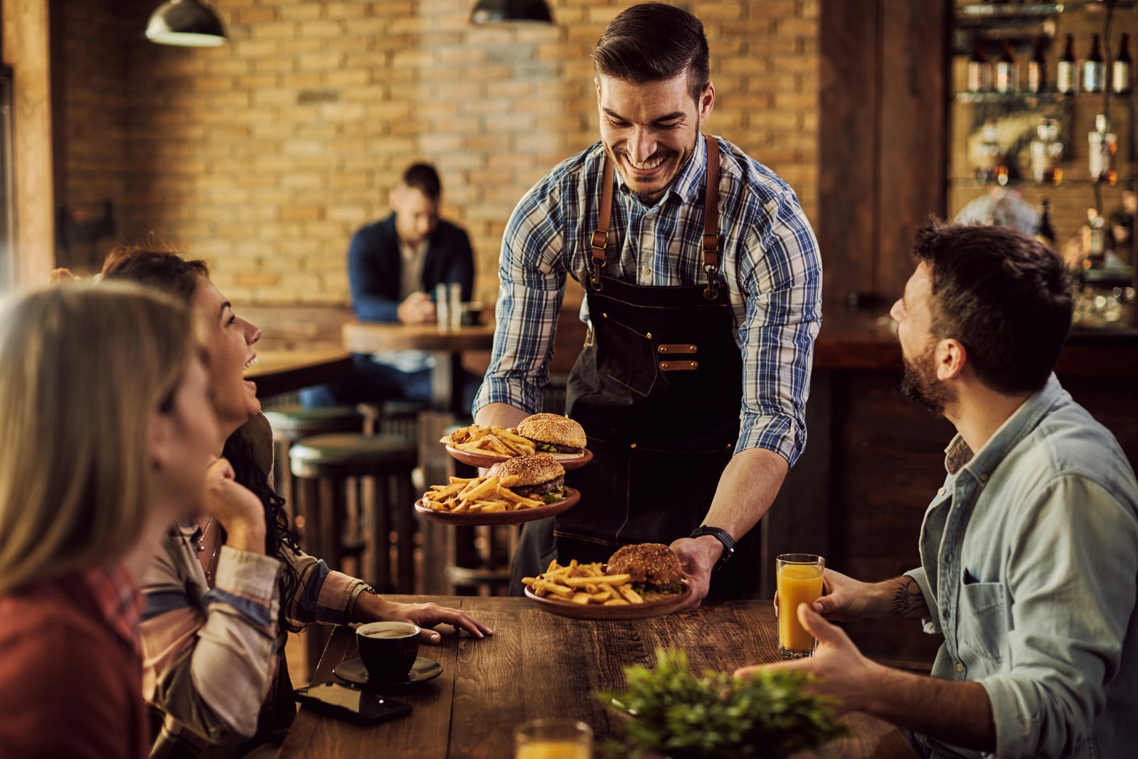 Happy waiter serving food to cheerful friends at pub